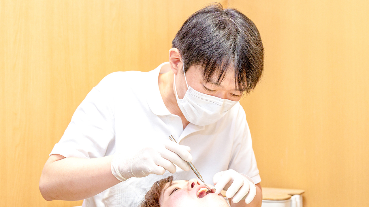 院長が診療室で患者の口の中を診察している写真